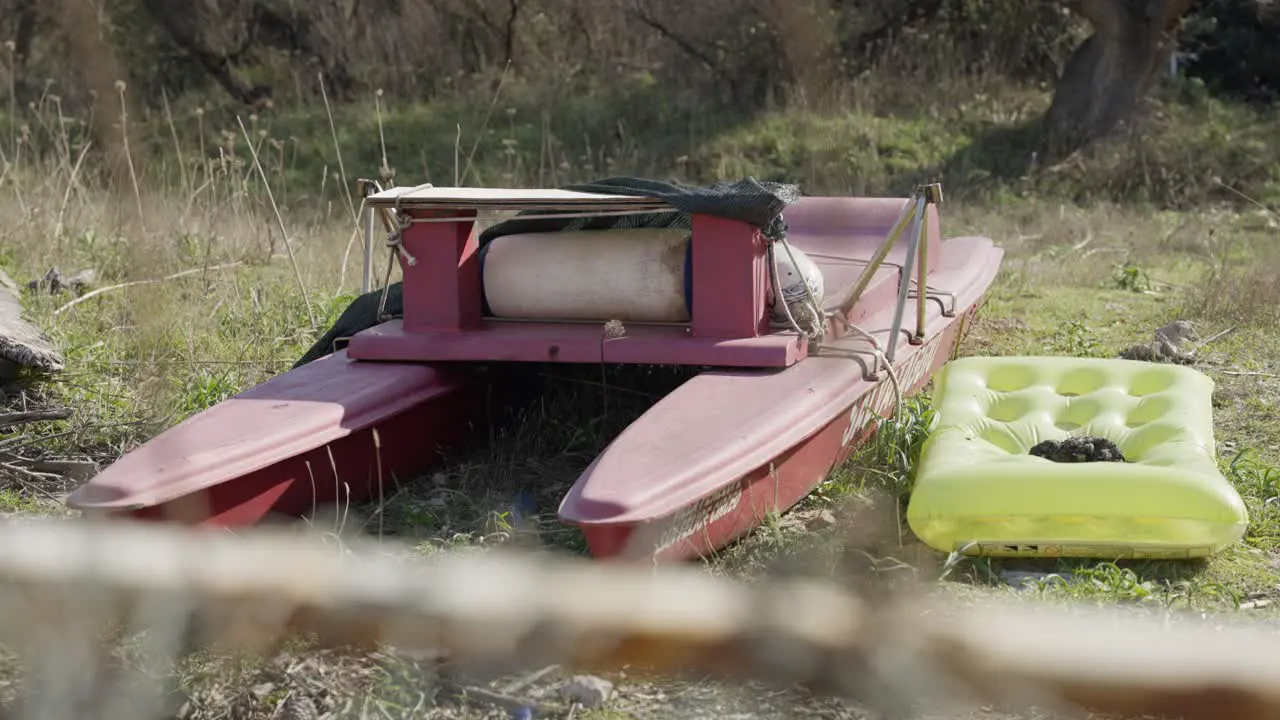 Abandoned Red catamaran left on the side with a yellow air mattress next to it in the nature of Sabaudia in Italy on a sunny day