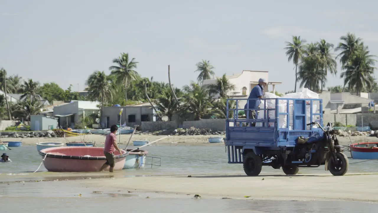 Fishermen unloading bags of motorbike cart and placing on coracle boat