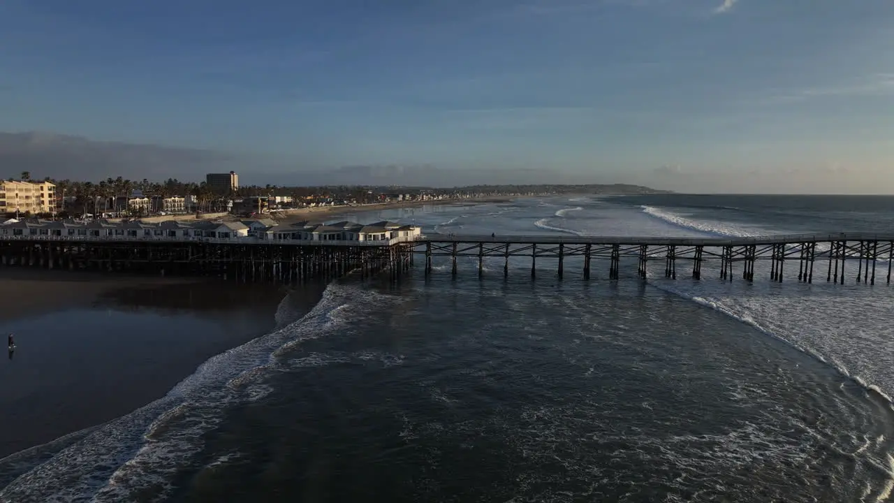 Drone shot along ocean beach approaching then passing over pier at dusk