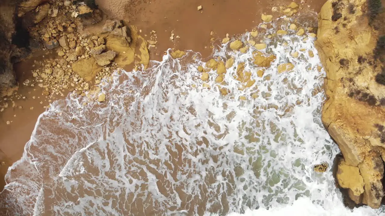 Aerial top view of ocean waves break on a rocky sand beach