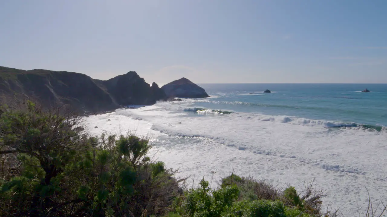 mountainside view of waves rolling in along the shores of Big Sur California beach Pacific Ocean