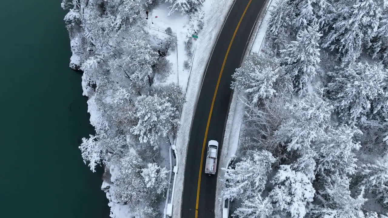 Top down shot of a truck driving near a body of water with snow covering the land