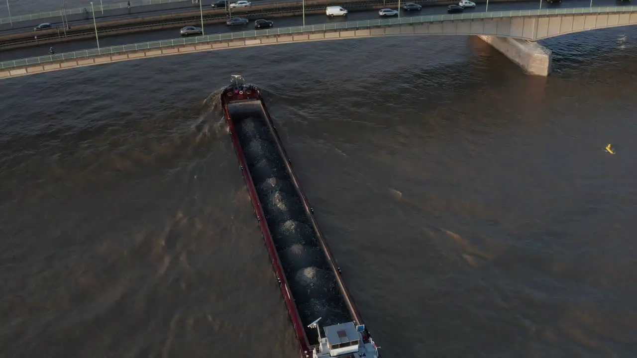 High angle view of loaded cargo ship passing under busy road bridge at golden hour Cologne Germany