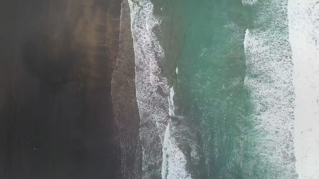 Birds eye view of ocean waves crashing into a black sand beach