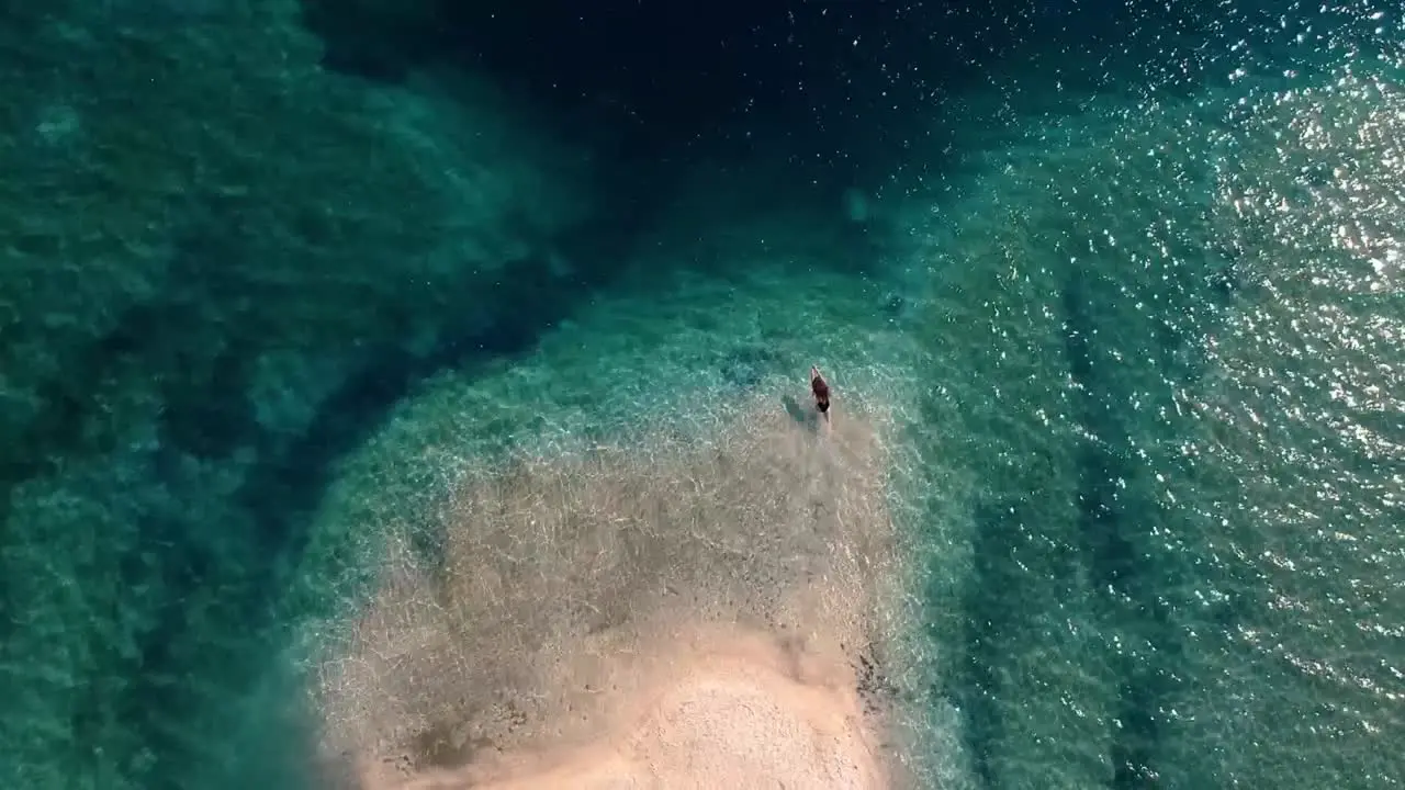 Female Tourist On A Stunning Island In Italy Diving Into The Shallow Blue Sea With Crystal Clear Water aerial top view