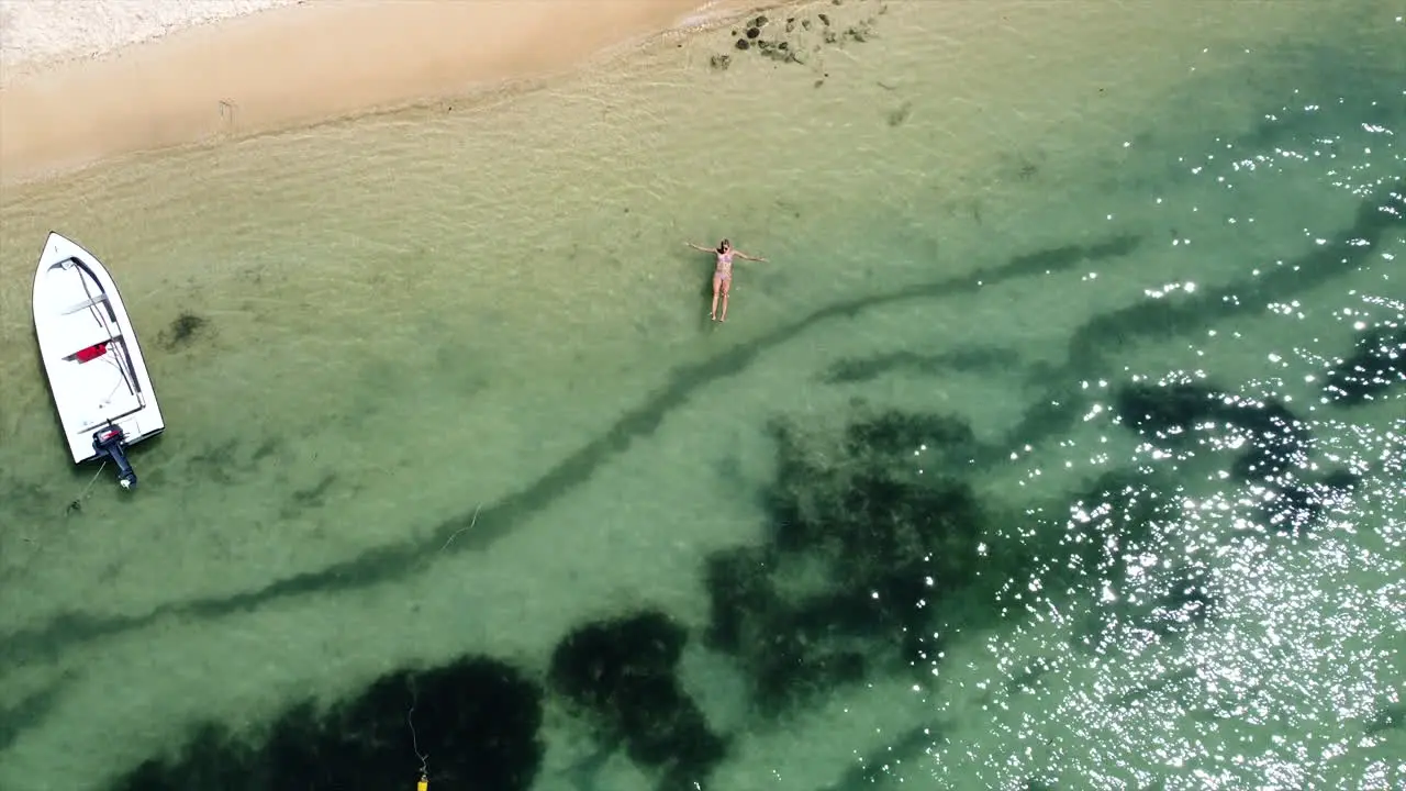 Descend aerial drone shot of woman lying in crystal clear ocean on sunny day