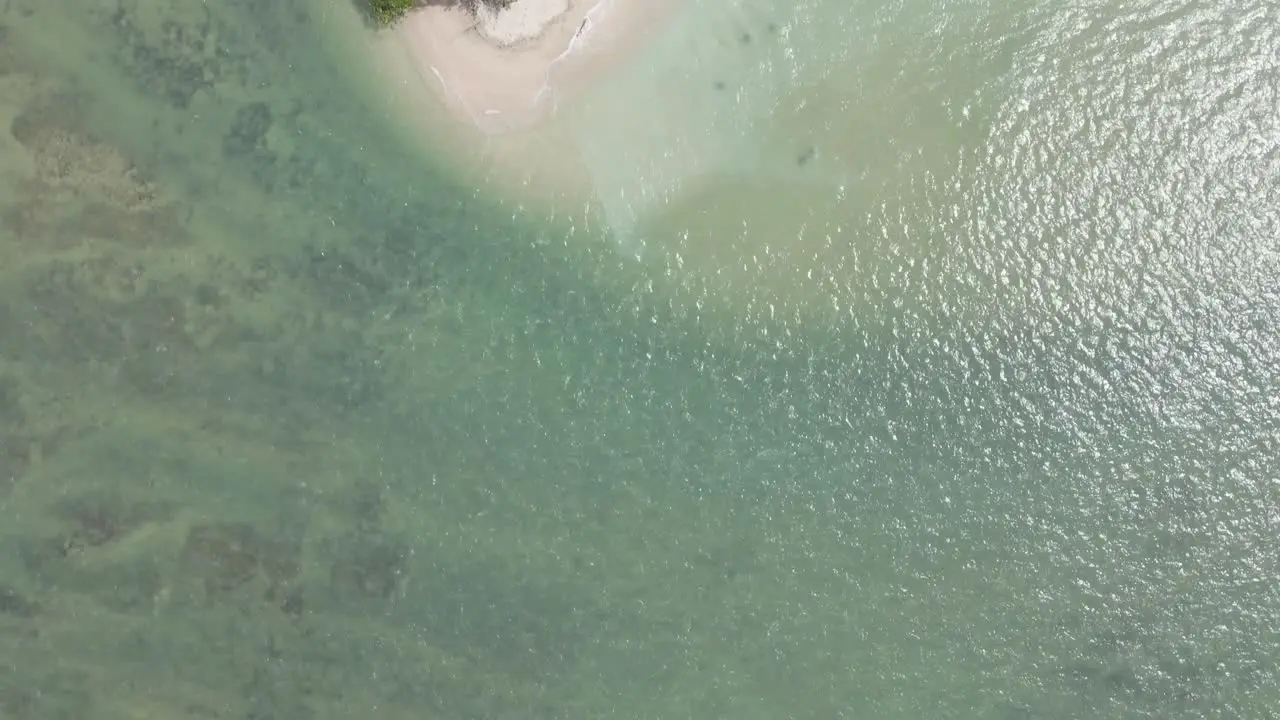 Drone flies over clear sea onto lush green island