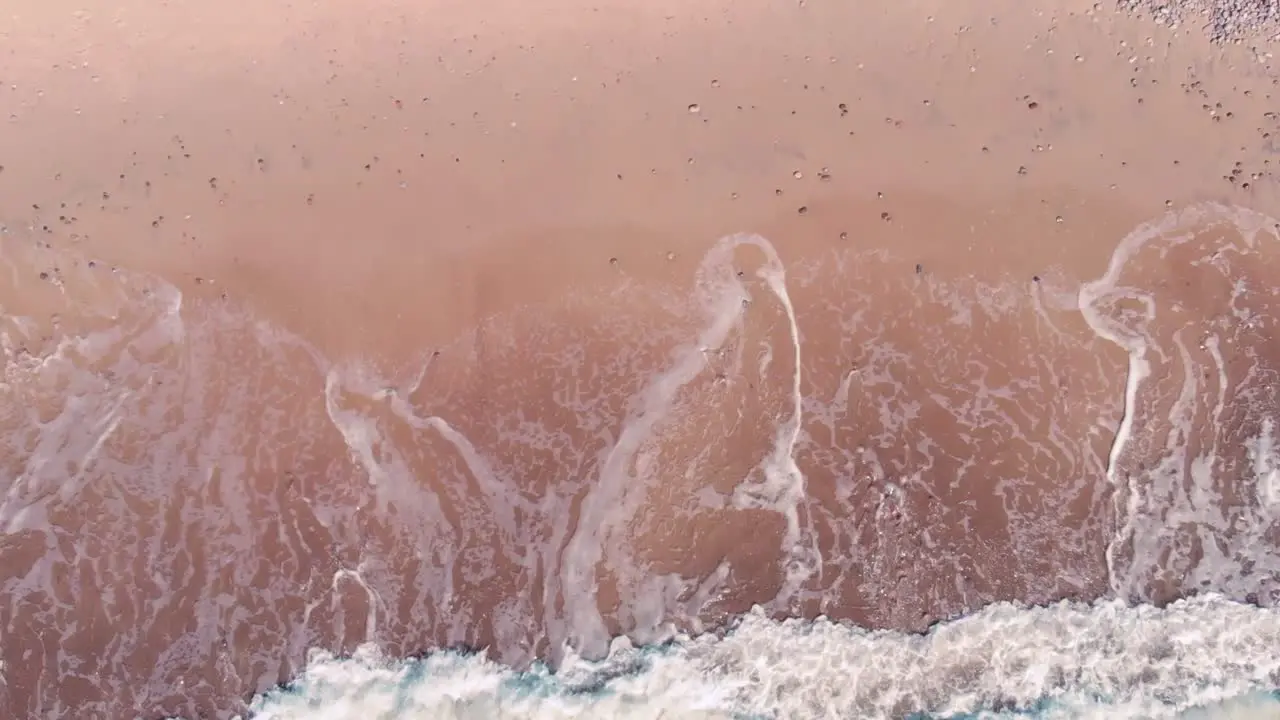 Overhead top down view of tropical pink beach with wave creating white foam