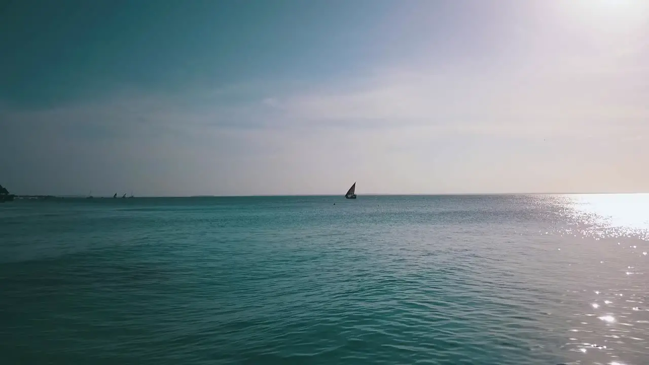 Buttery soft aerial flight slowly rise up drone shot from a sailboat far out at sea sun reflection