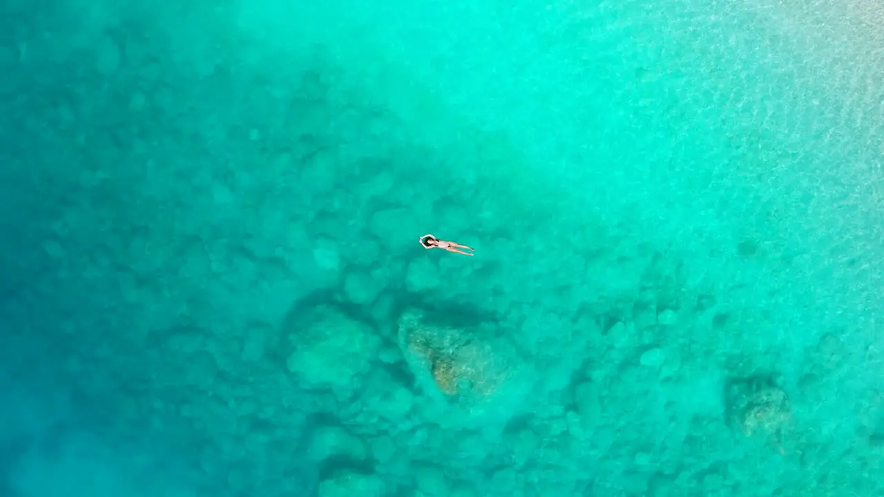 Top down Aerial of a Girl Floating and Lying in paradise Turquoise Ionian Sea in Greece Myrtos Beach