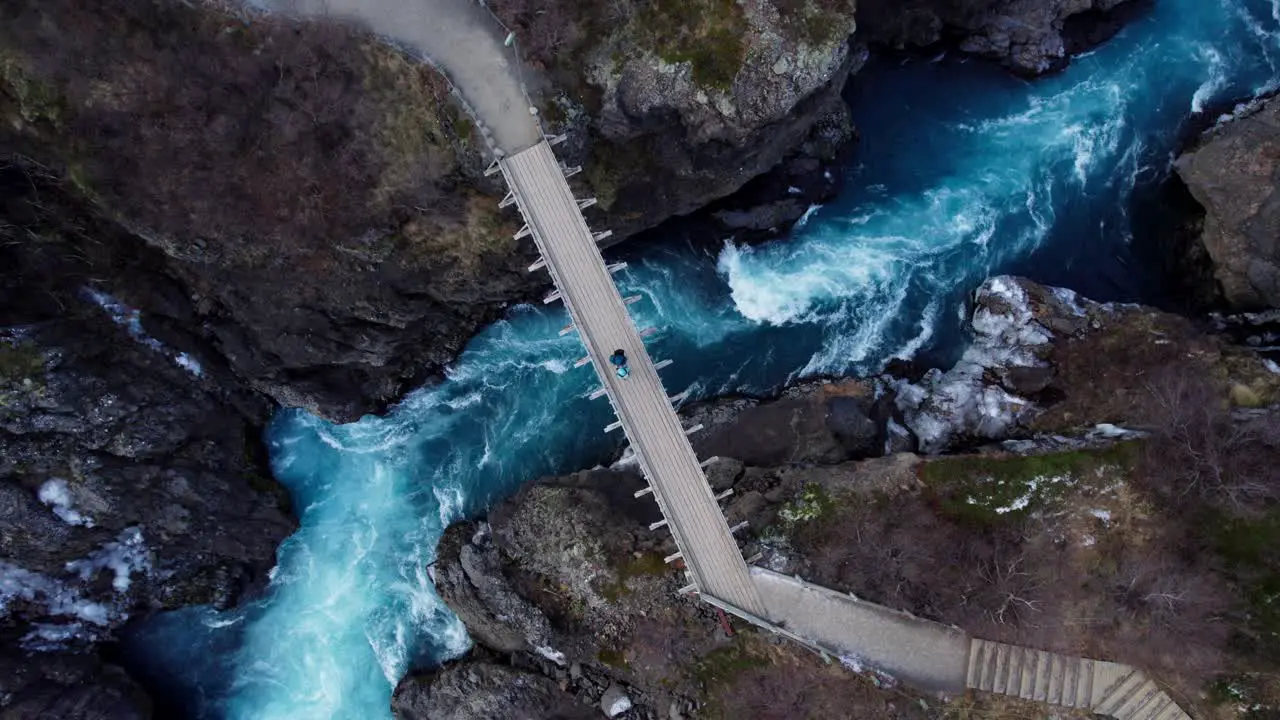 Couple standing on impressive bridge over wild river and waterfall in volcanic landscape Aerial top down rotate