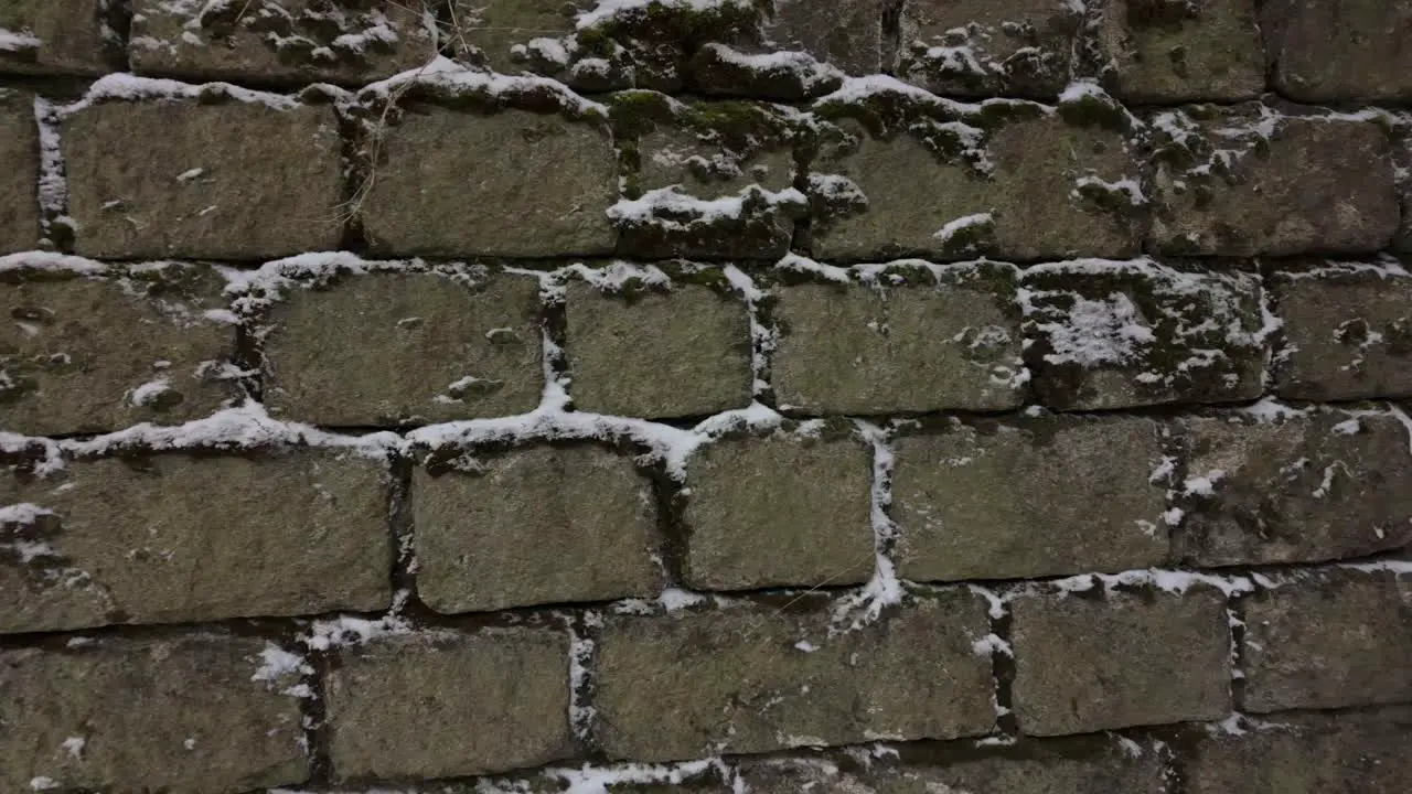 Close-up of an old stone wall with moss grown between the stones covered in snow