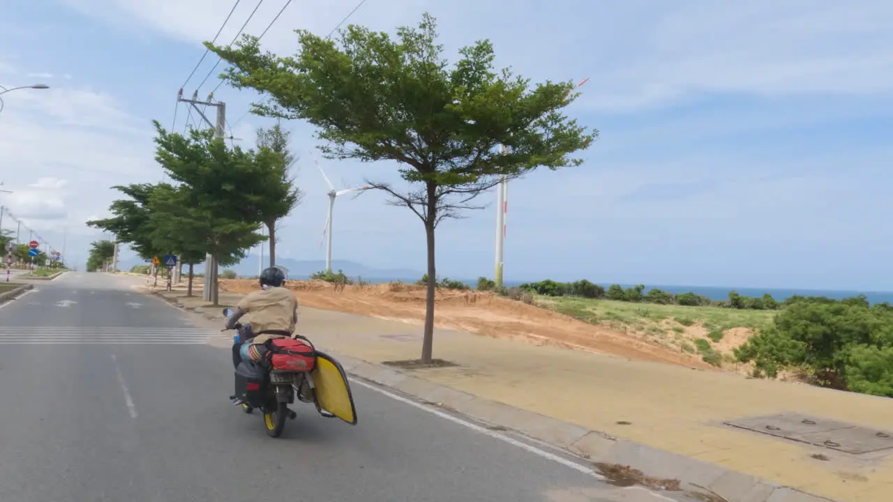 Man riding motorbike carrying surfboard in Indonesia follow back view