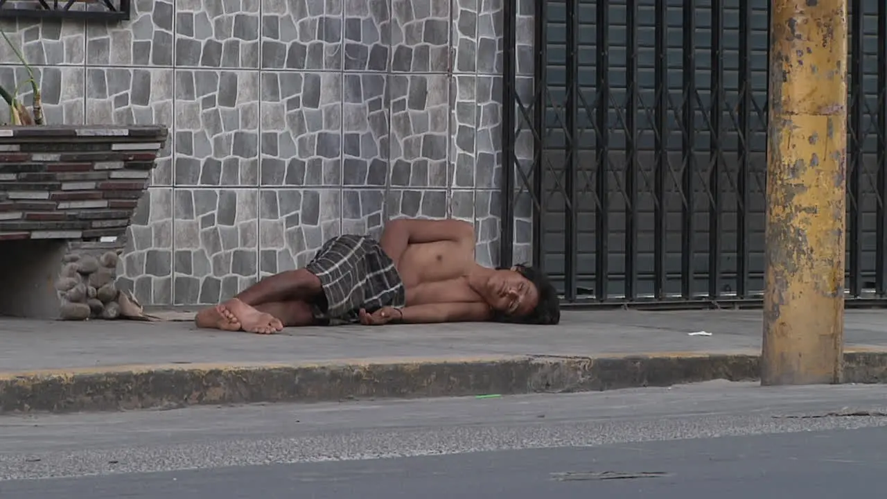 View Of Homeless Adult Topless Male Sleeping On Pavement With Traffic Going Past