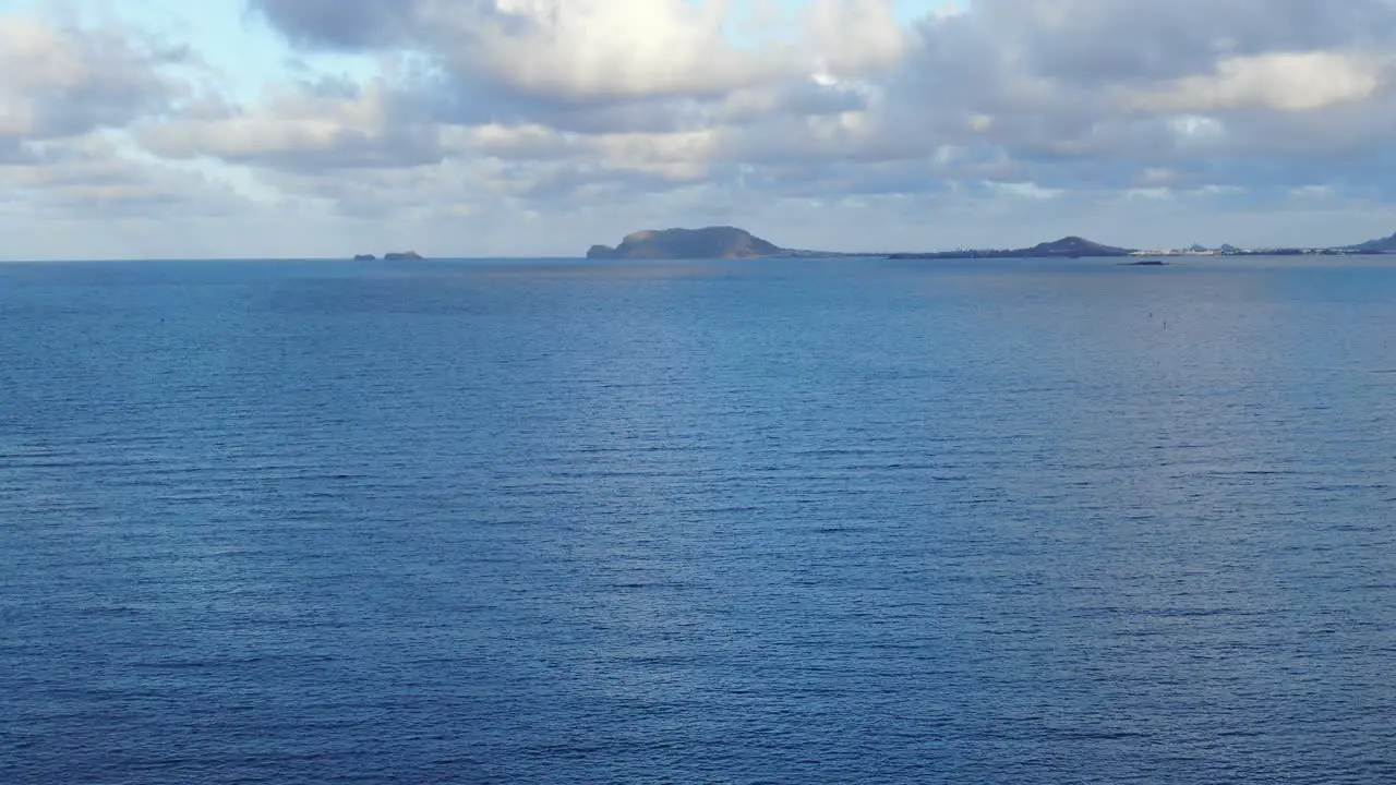 A static shot of calm water of deep blue ocean with clouds and sun reflection