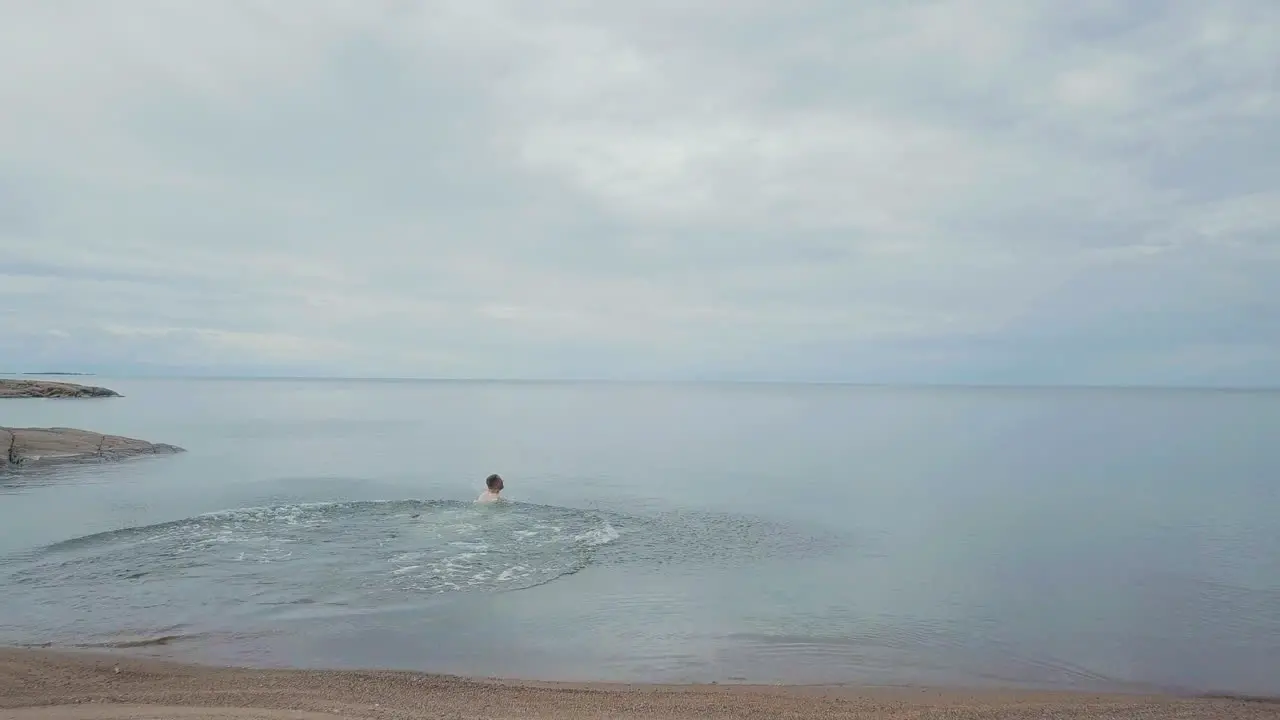 Tracking Aerial Man runs on beautiful ocean beach and dives into calm water