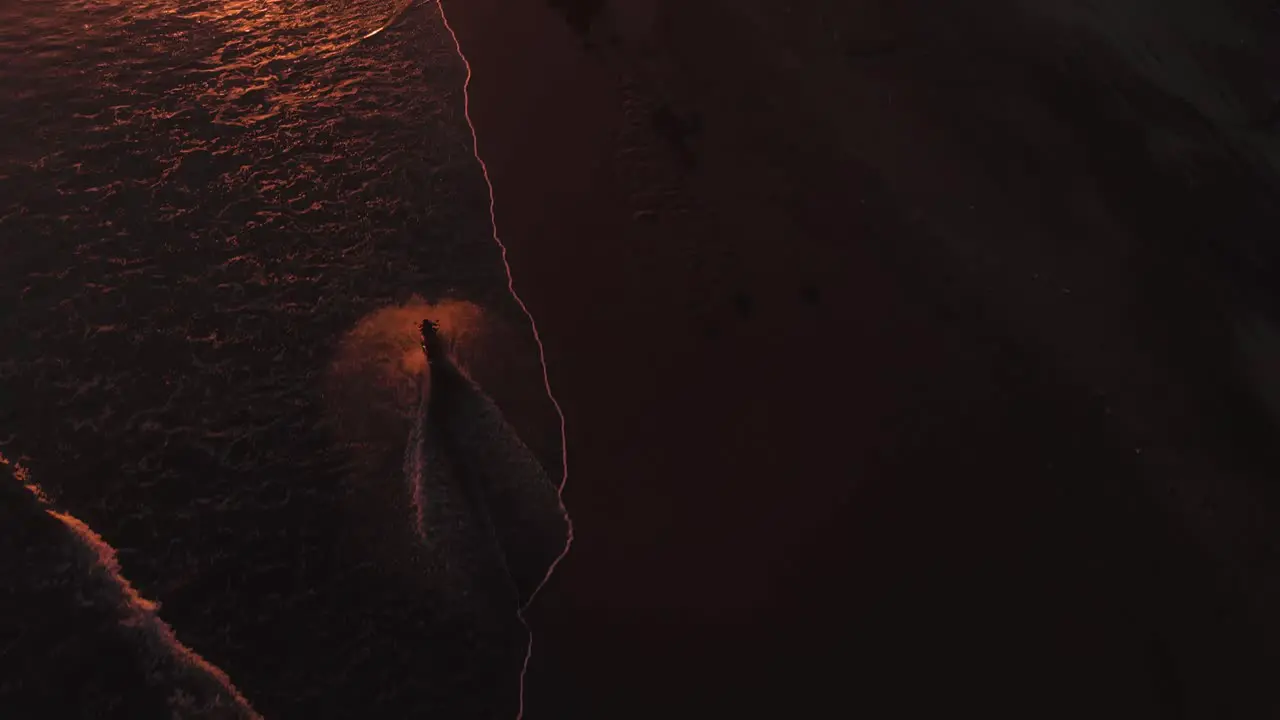 Bir eye view of a woman riding motorcycle towards the sunset on the beach riding in the water at Pasut Beach Bali Indonesia