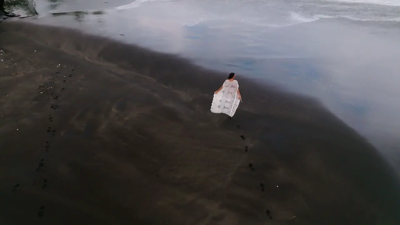 Aerial drone shot of young woman walking on black sand beach in Bali Indonesia