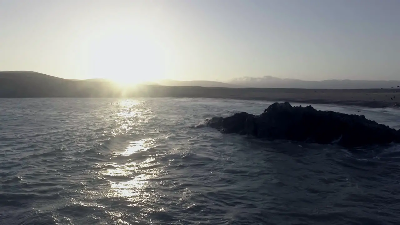 Amazing zoom out drone shot of the sea during sunset as the waves crash against the rocks