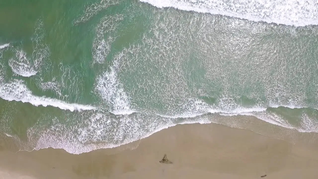 Birds eye view of a light blue sea breaking in a sandy beach