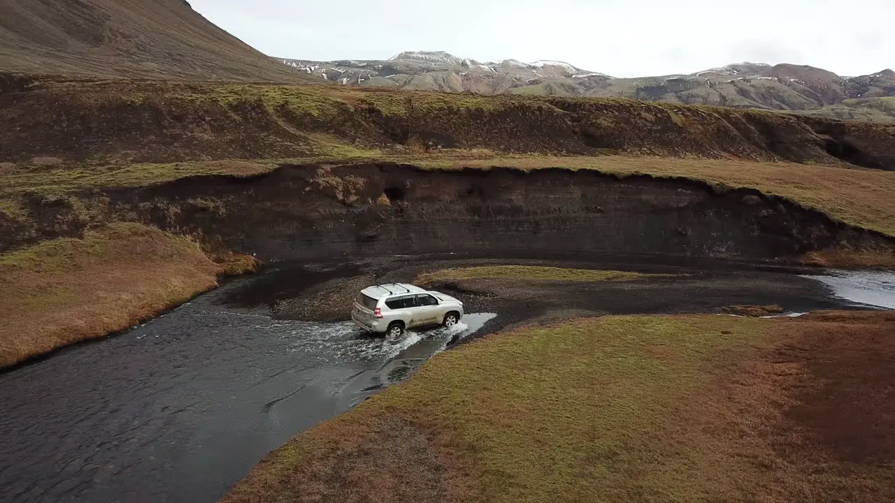 Four Wheeler on Rough Offroad and Shallow River in Iceland Countryside Under Volcanic Hills Aerial View