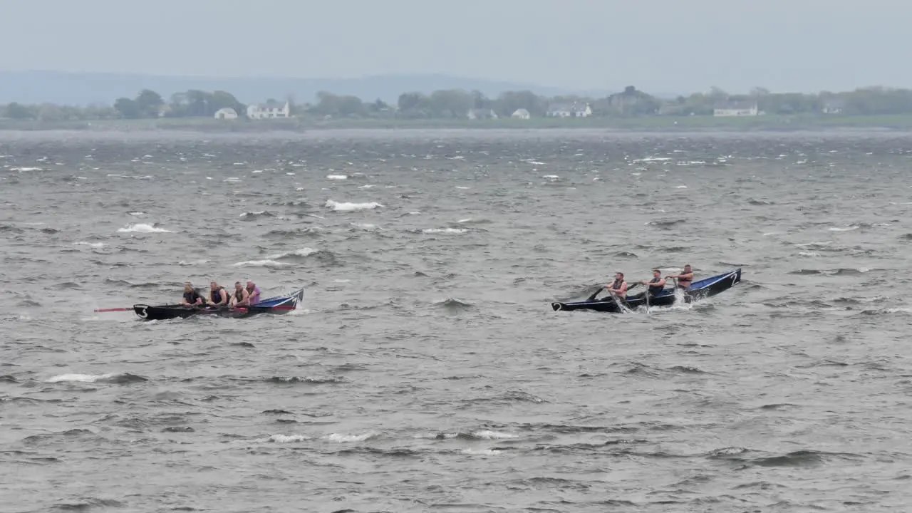 Tracking pan follows currach boats rocking over rough sea waves county clare behind