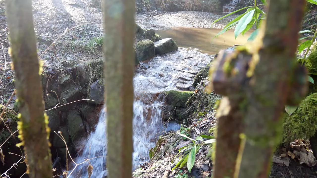 Small cascading rock waterfall copper coloured pool flowing behind metal railings closeup dolly left