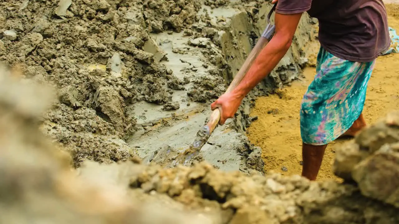 Barefoot Bangladesh man shovels wet soil for use in brick field