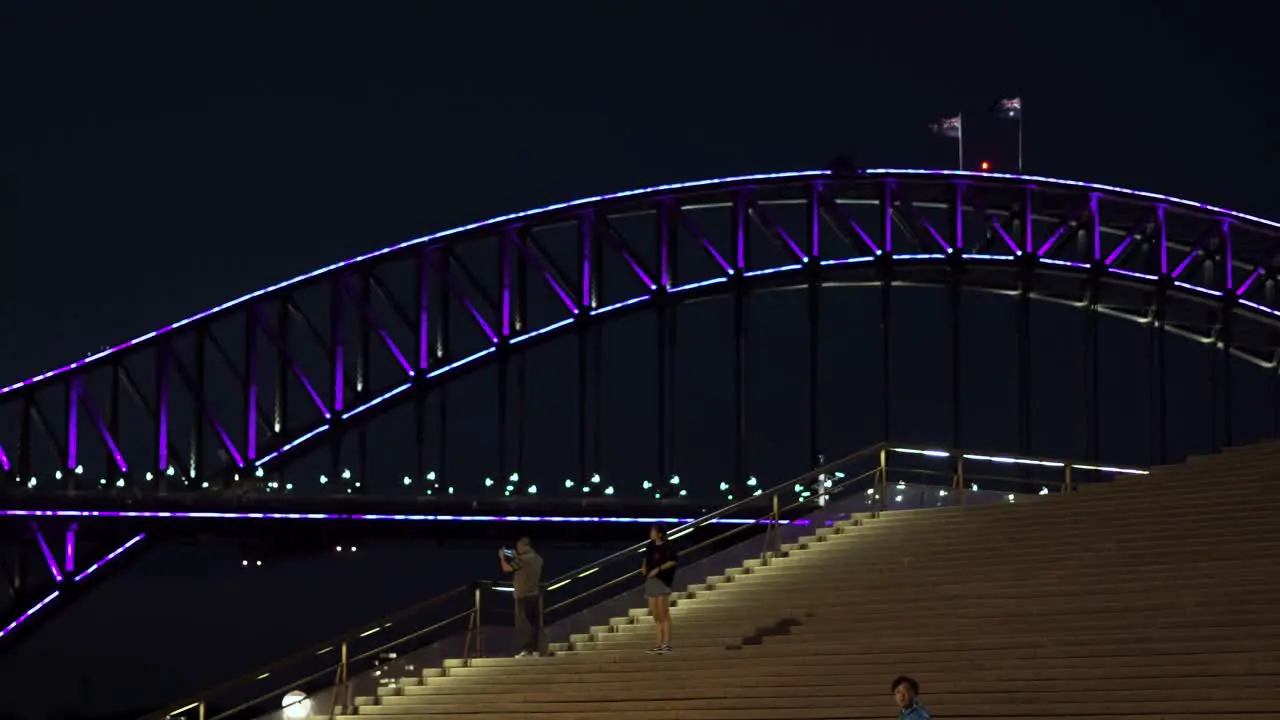 Left-sliding shot revealing the Sydney Harbour Bridge lit up at night