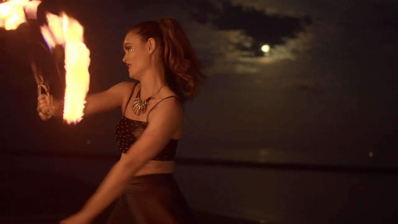 Woman Dancing And Twirling With Fire Fans Against a Cloudy Full Moon Lit Night Sky Medium Shot Slowmo