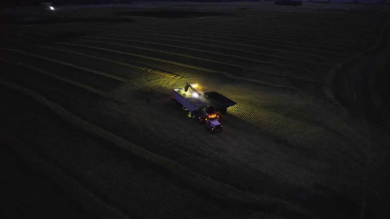 Grain unloaded onto semi truck with trailer at night in farm land aerial