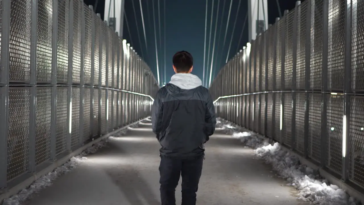 Young white male walking away from camera on a pedestrian bridge at night