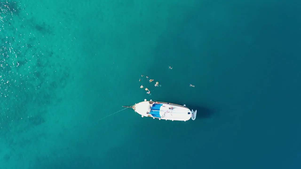 People swimming in sea beside luxury yacht aerial top down view