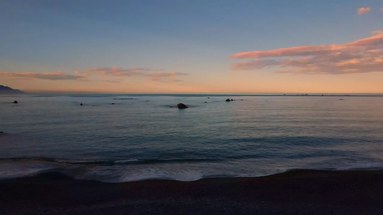 Rising drone shot out to sea at dusk with rocks in the water