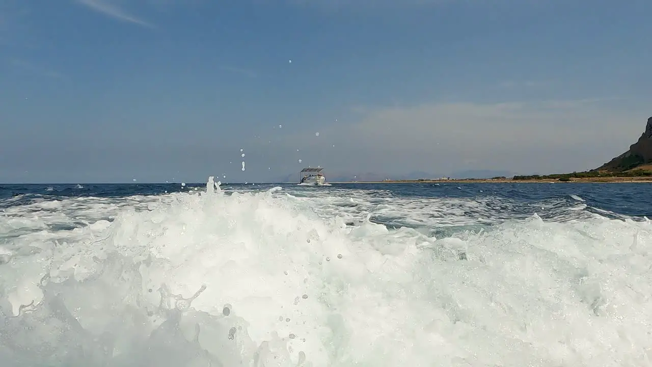 Low-angle water surface pov of boat wake trail with Riserva dello Zingaro natural reserve of Sicily in background