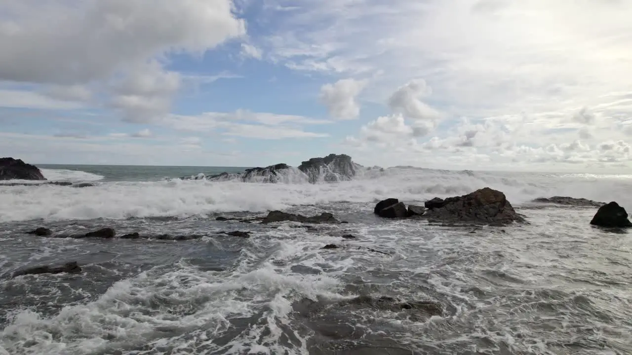 Aerial dolly in flying over foamy sea waves hitting the rugged shore on a cloudy day in Dominicalito Beach Costa Rica