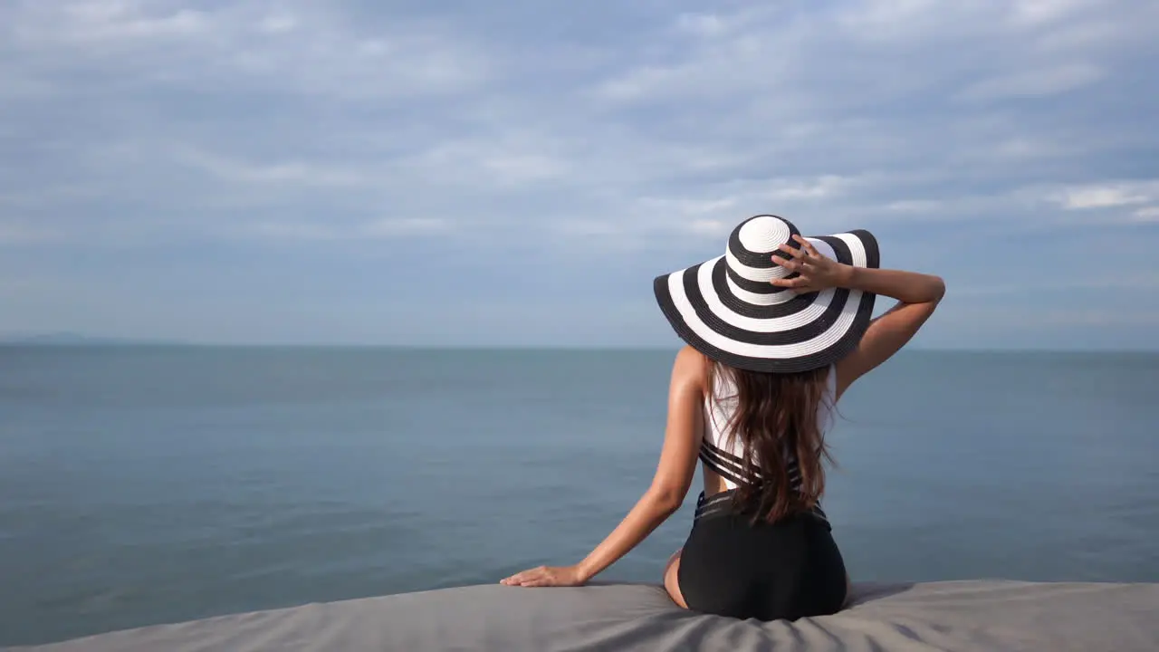 Young slim woman in bathing suit and hat looks out at sea and scans the horizon