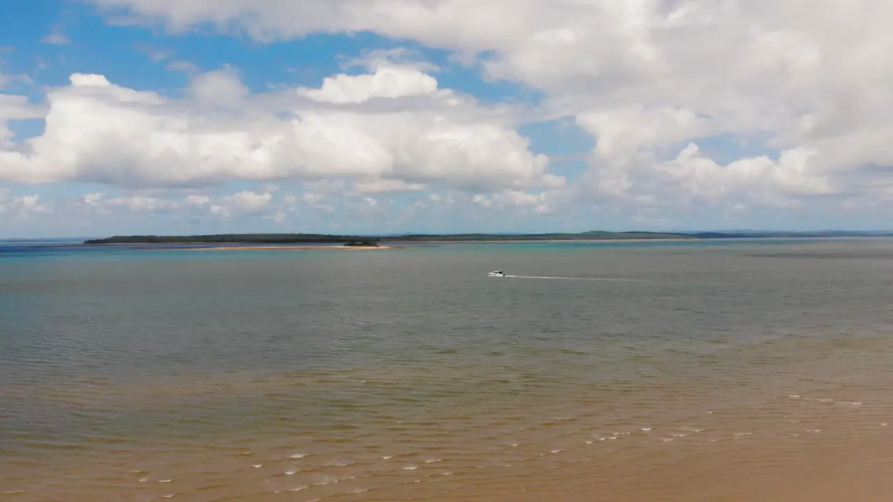 Slow push towards a boat gently sailing between two tropical islands on a gorgeously sunny day where the blue sky above features many large fluffy white clouds that float overhead