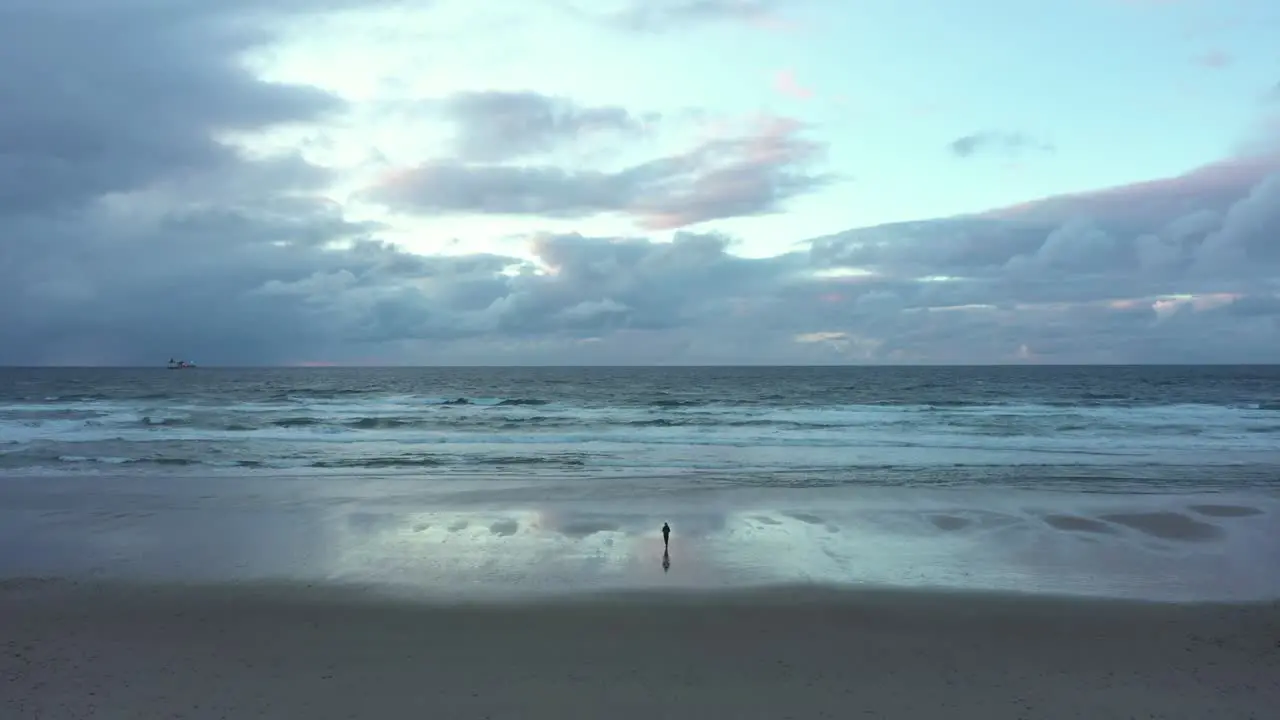 Aerial view of a man on wet beach calm before the storm descending drone shot