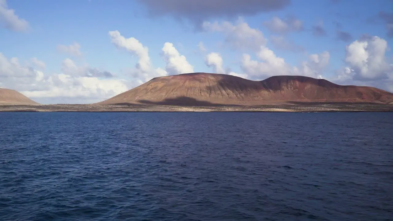 Shot taken from the sea looking towards the shore where there are arid and dry brown lands that form mountains taken during a sunny day with clouds