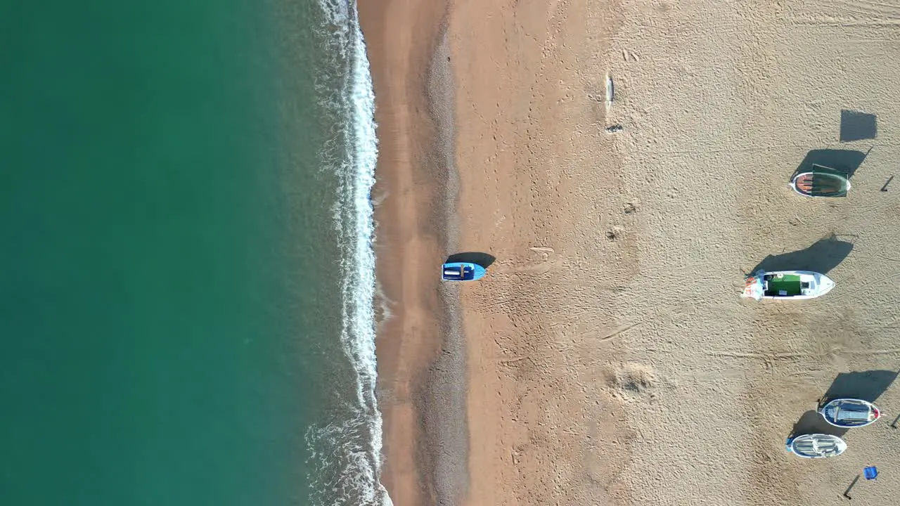 Aerial overhead view of a beach with calm turquoise blue waters fishermen boats in the foreground