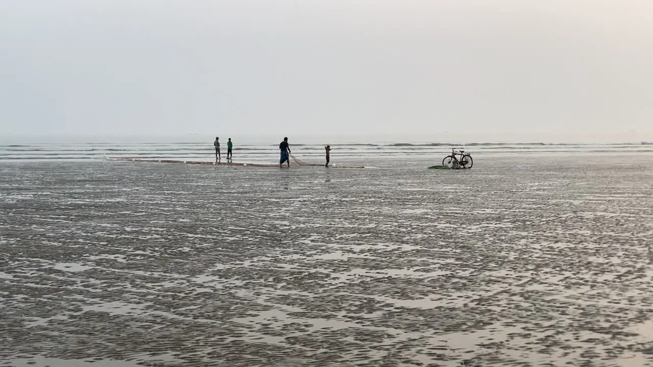 Silhouette shot of an empty beach with fisherman working on his net with his child and some people talking bike parked aside in Kolkata