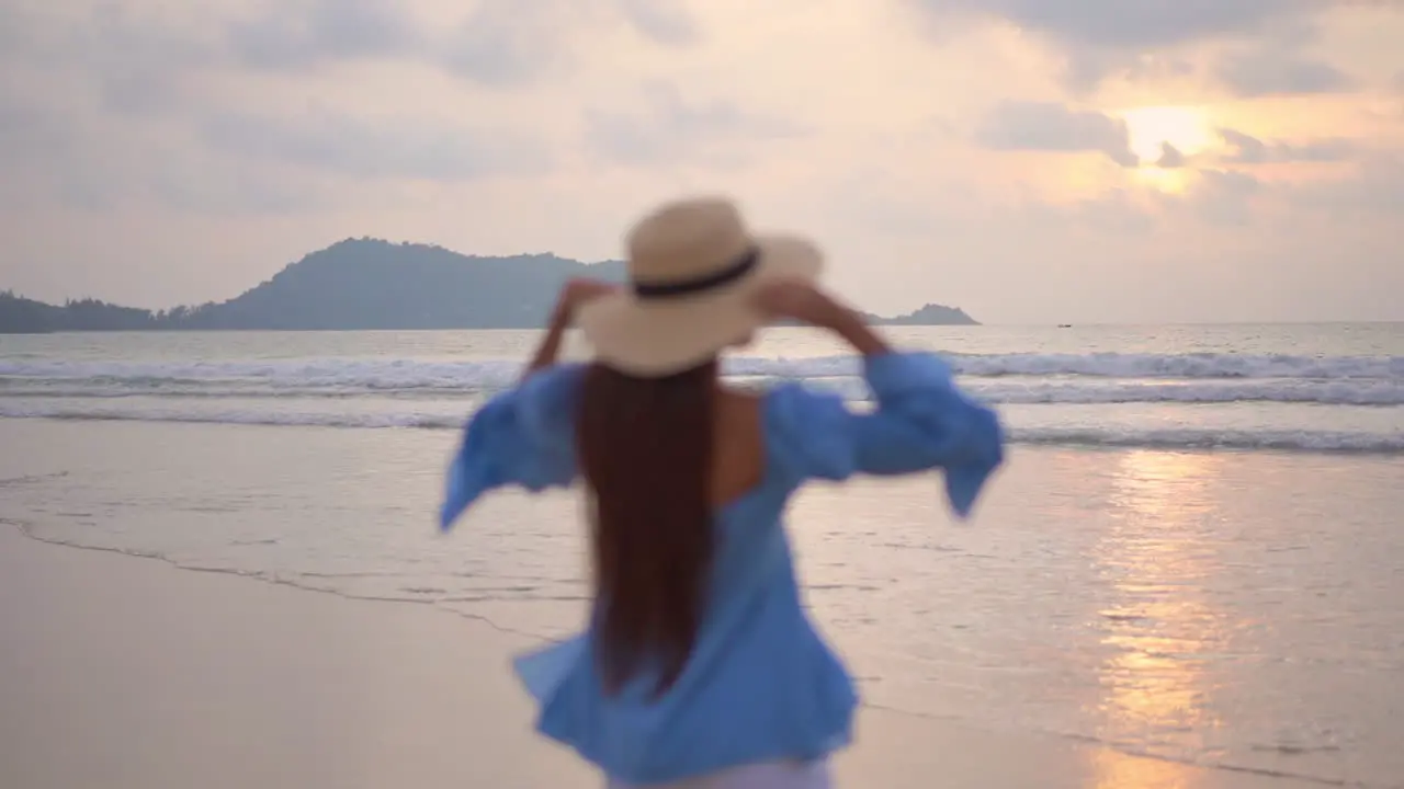 Young woman walks on seashore at sunset and raises her arms