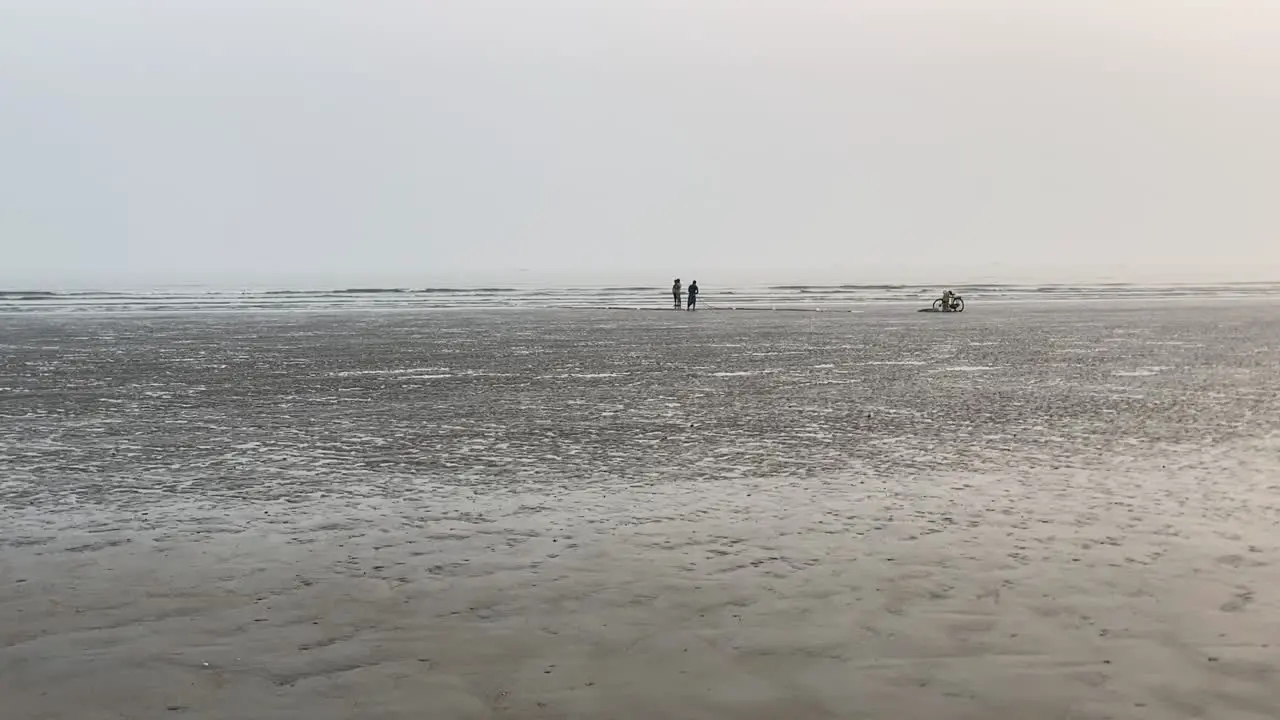 POV walking shot of an empty beach with fisherman and his only son working on their fishing net in front of sea waves